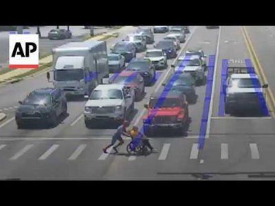 Man dressed as Spider-Man helps a person in a wheelchair cross the road